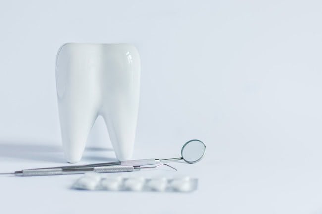 Model of white tooth, medical pills and dentistry tools on white background